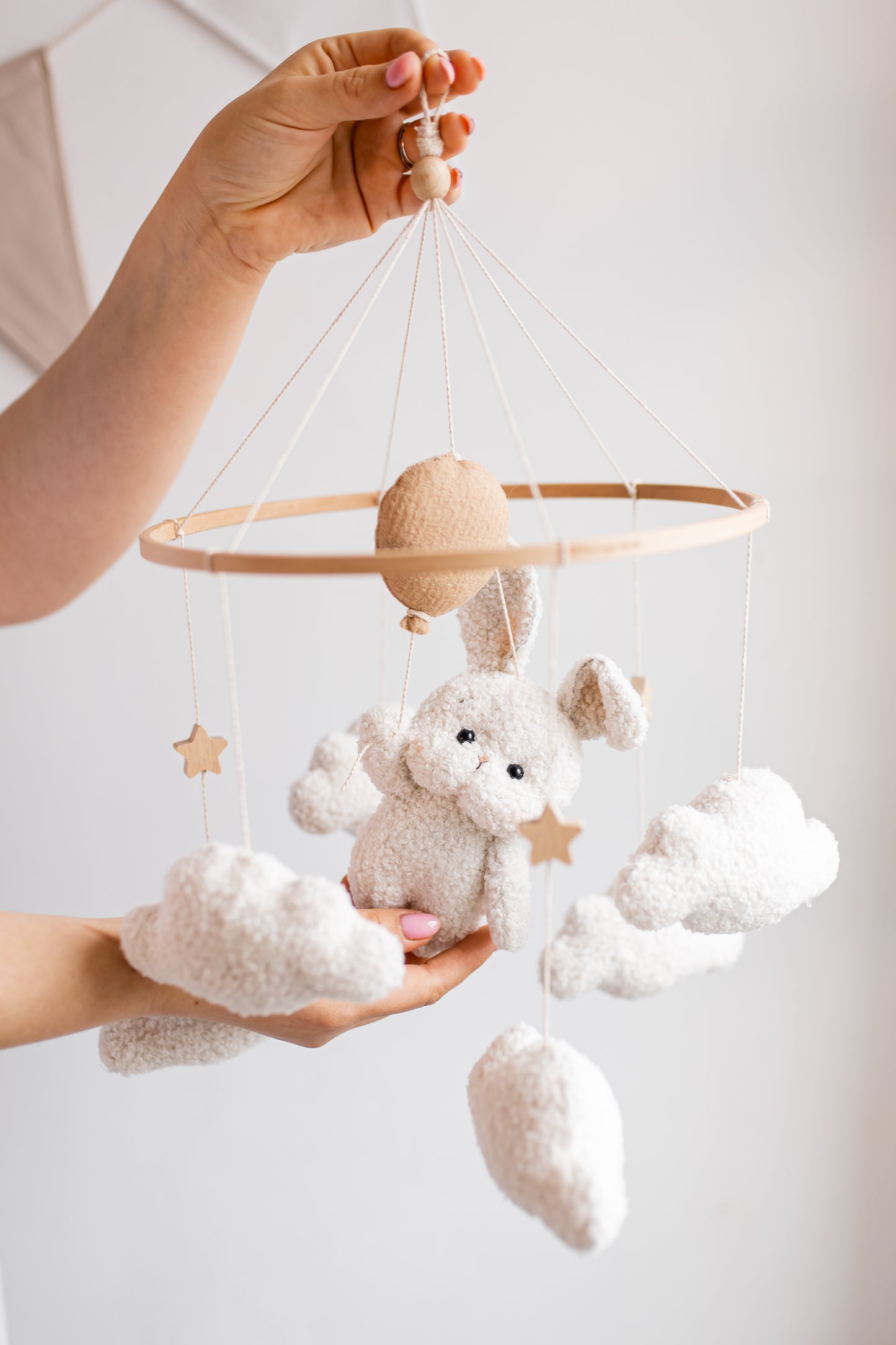 Baby mobile with plush toys held by a hand against a light background