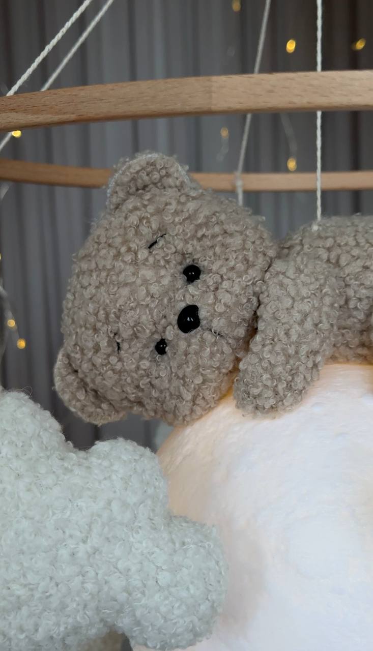 Close-up of a plush bear baby mobile decor toy hanging from a string with a neutral background