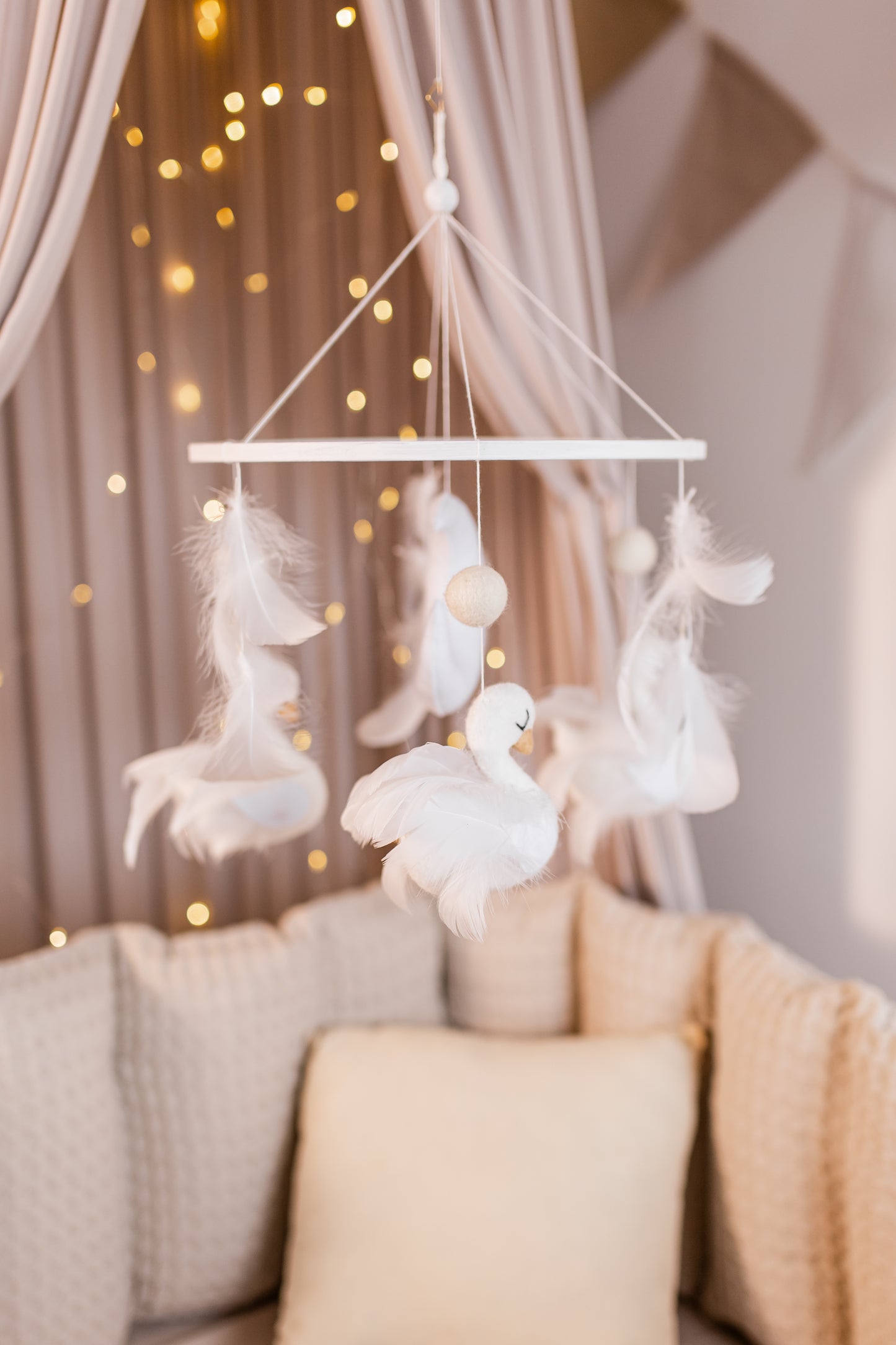 Decorative mobile with swan shapes hanging above a sofa with soft lighting in the background.