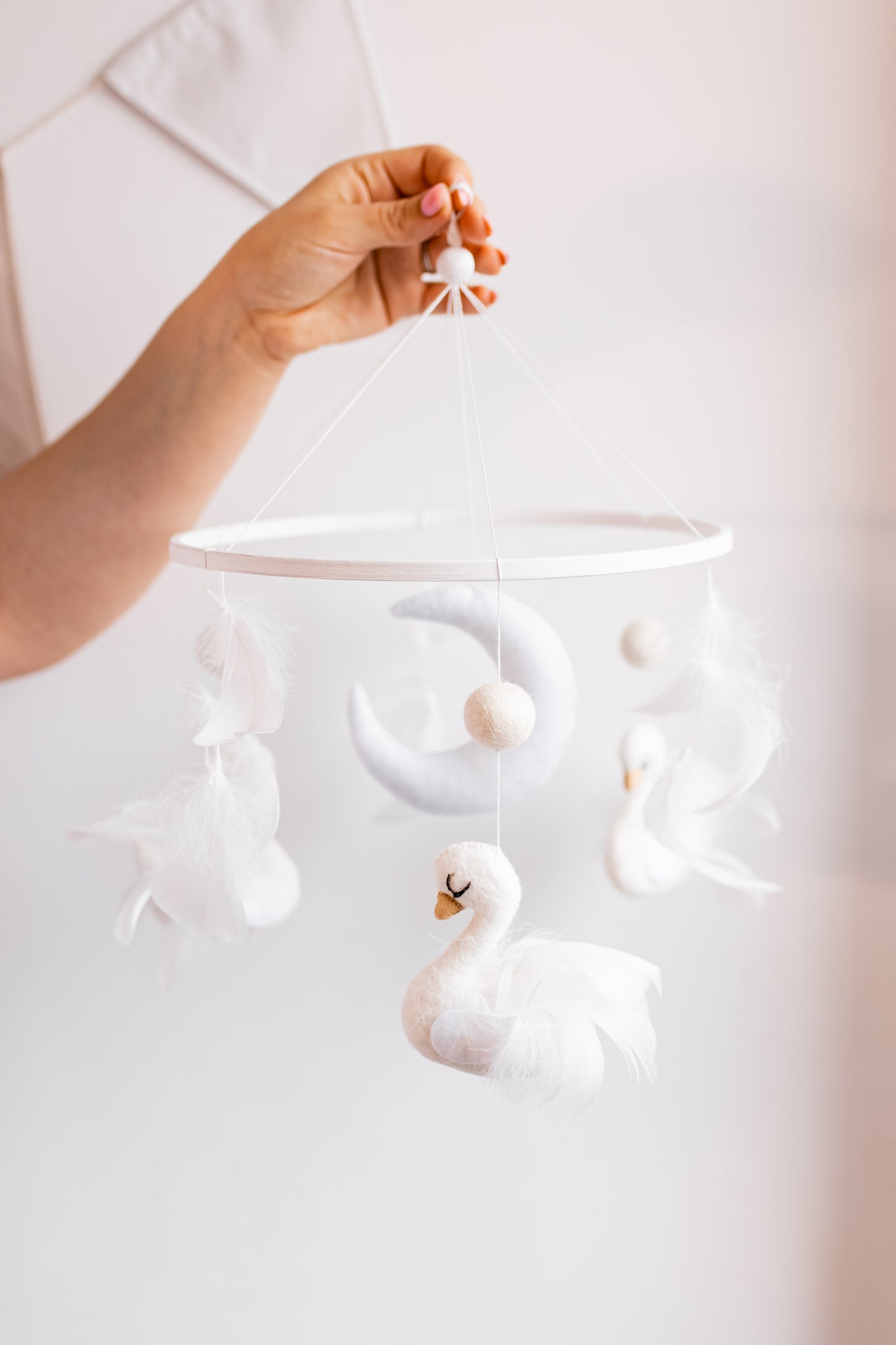 Hand holding a white swan-shaped baby mobile against a light background