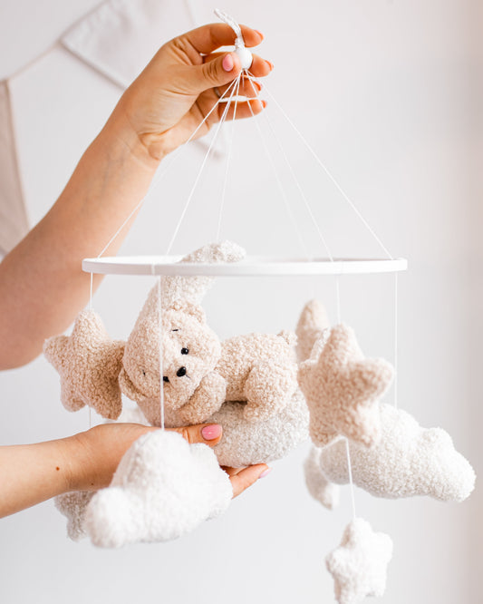 Hand holding a baby mobile with teddy bears and stars against a white background