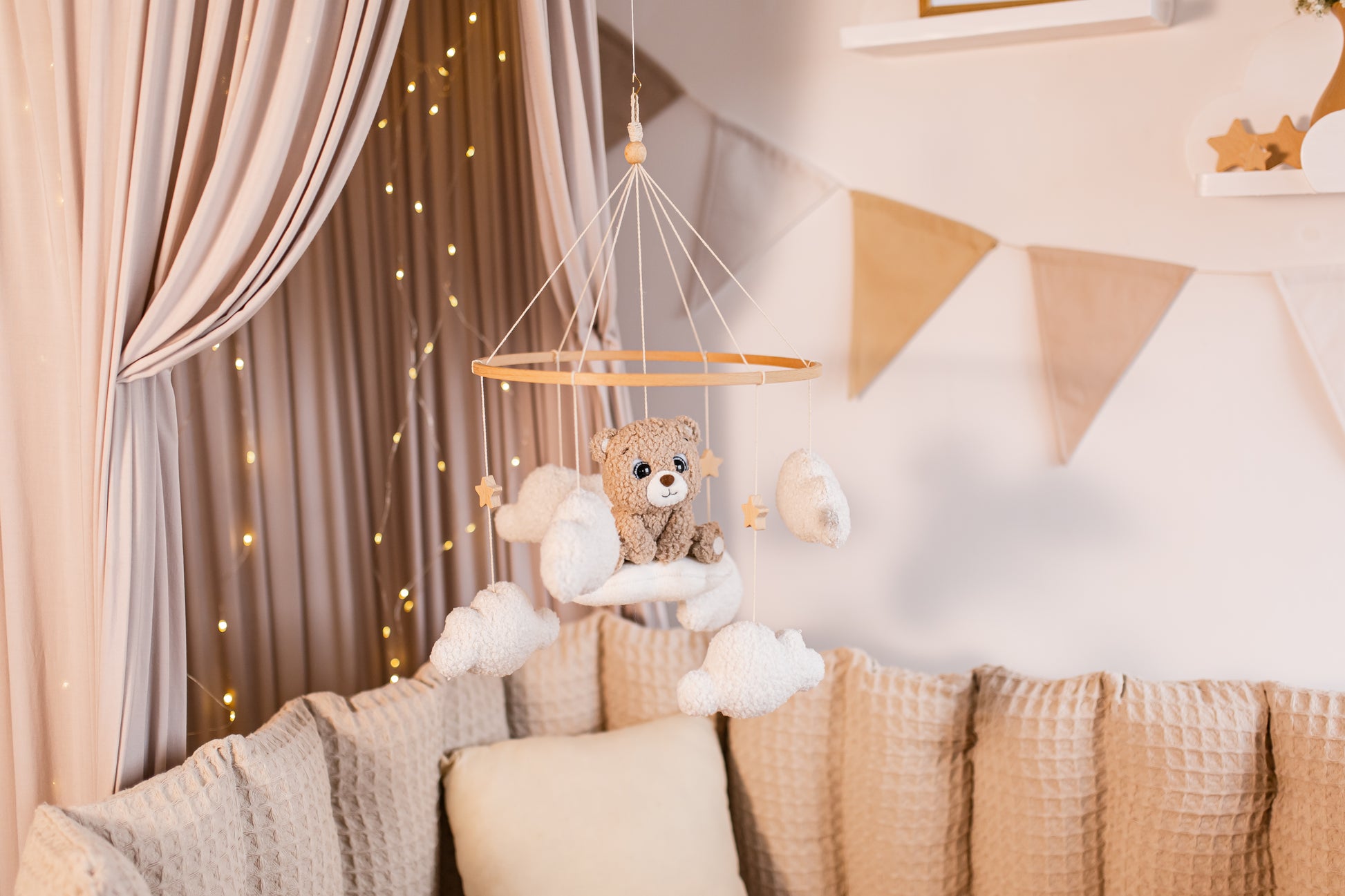 Baby crib mobile with teddy bear and clouds hanging above a crib in a nursery.