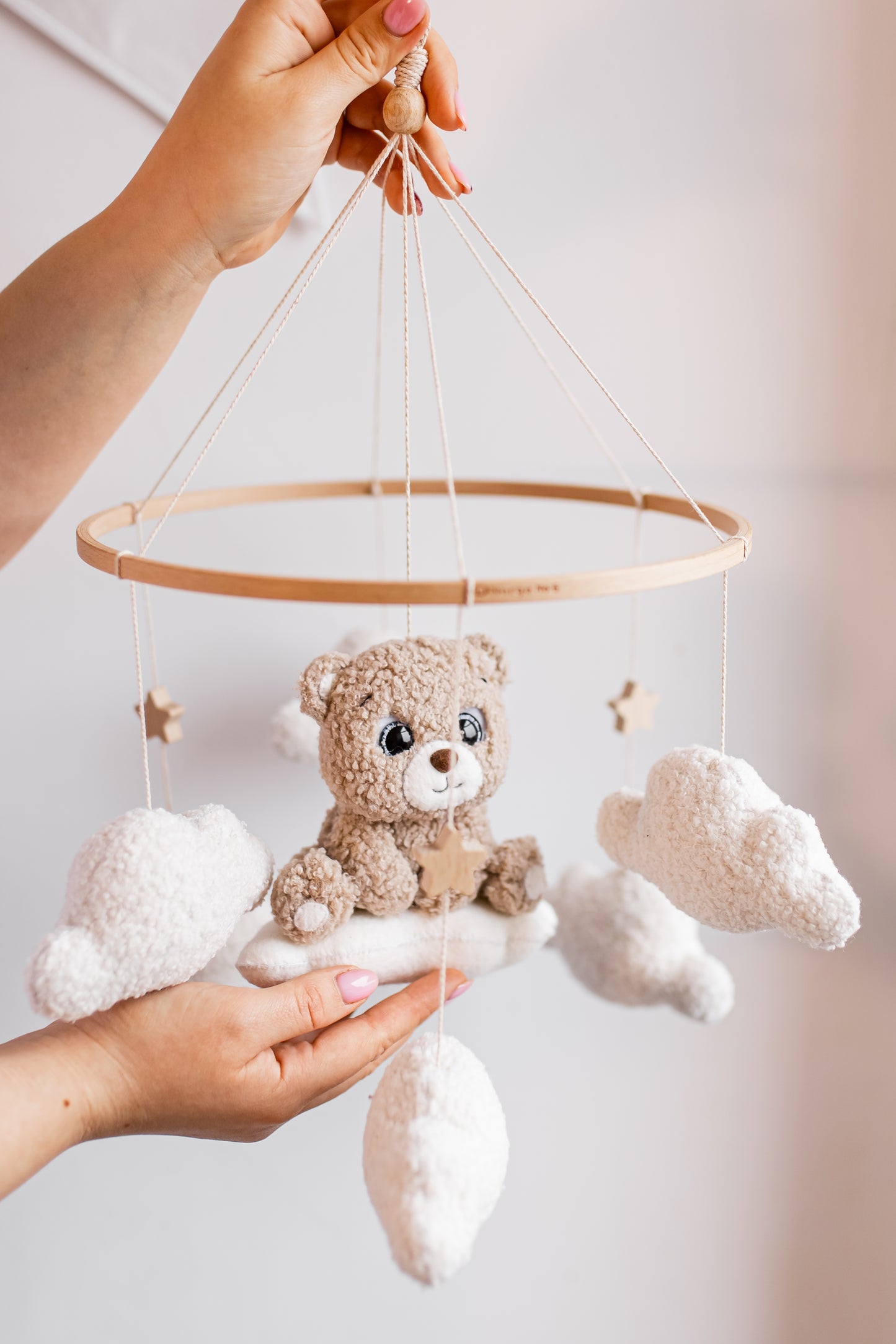 Handmade toy mobile with teddy bear and clouds held by a person against a plain background